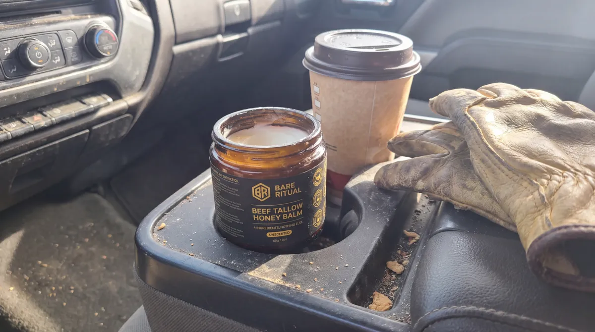 A jar of Bare Ritual in a truck cup holder next to coffee and work gloves